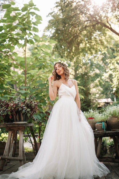 Belle fille en robe blanche avec une guirlande de fleurs sur sa tête est debout en plein air