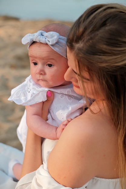 Une belle fille en robe blanche avec un nouveau-né est assise sur la plage sur le sable