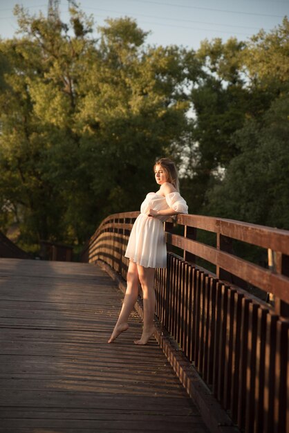 Une belle fille en robe blanche se dresse sur un pont en bois