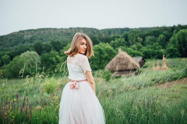 Belle fille en robe blanche se trouve dans l'herbe verte