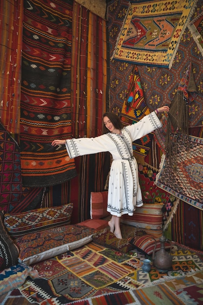 Belle fille en robe blanche avec une théière dans un intérieur turc traditionnel avec de nombreux tapis au mur