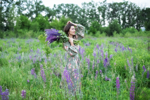 belle fille en robe avec un bouquet de lupin se dresse dans un champ de fleurs en été