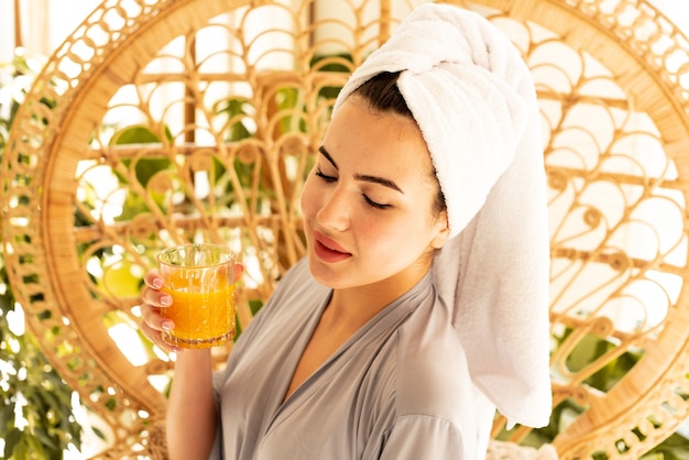 Une belle fille en robe de chambre boit du jus d'orange. Elle accueille magnifiquement sa matinée en prenant soin d'elle