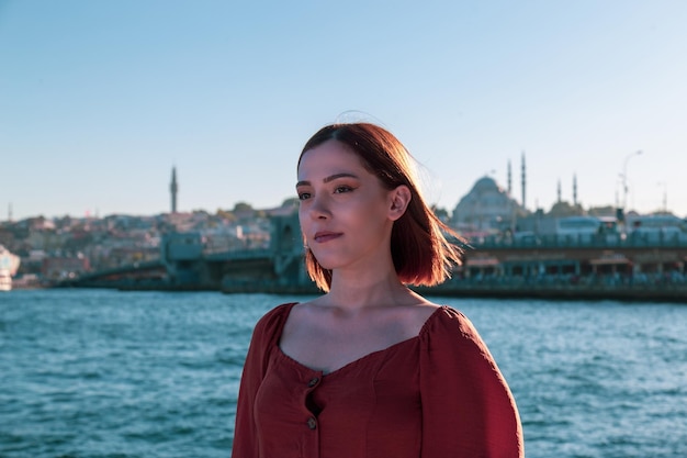 Belle fille avec une robe de couleur orange posant avec le pont de Galata et les mosquées d'Istanbul