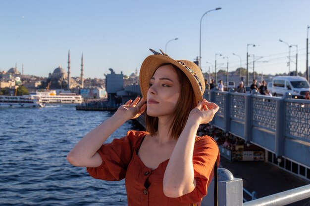 Belle fille avec une robe de couleur orange posant avec le pont de Galata et les mosquées d'Istanbul