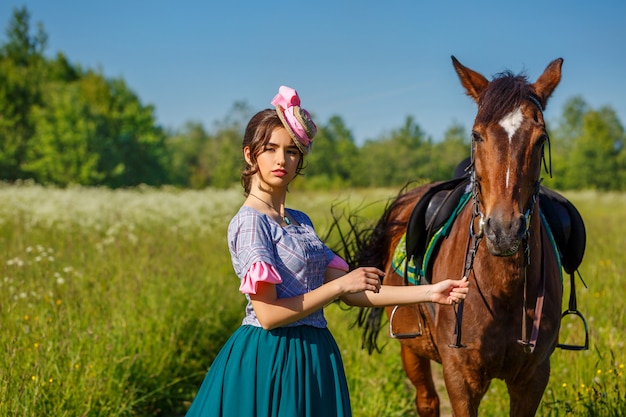 belle fille en robe debout avec un cheval dans la nature