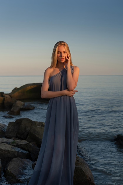 belle fille en robe grise au bord de la mer au coucher du soleil