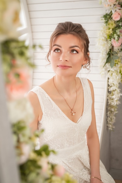 Belle fille en robe de mariée blanche est assise dans une fenêtre ronde