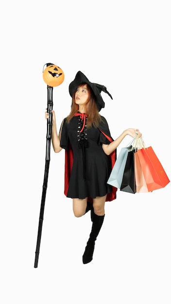 Belle fille en robe noire et chapeau de sorcière tient des sacs à provisions à la recherche d'une citrouille et tenant le personnel sur fond blanc concept d'Halloween