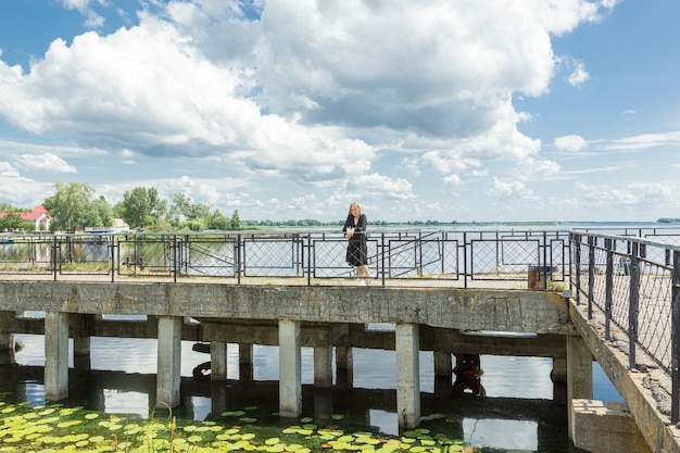 Belle fille en robe noire sur le fond de la mer fluviale avec ciel bleu et nuages