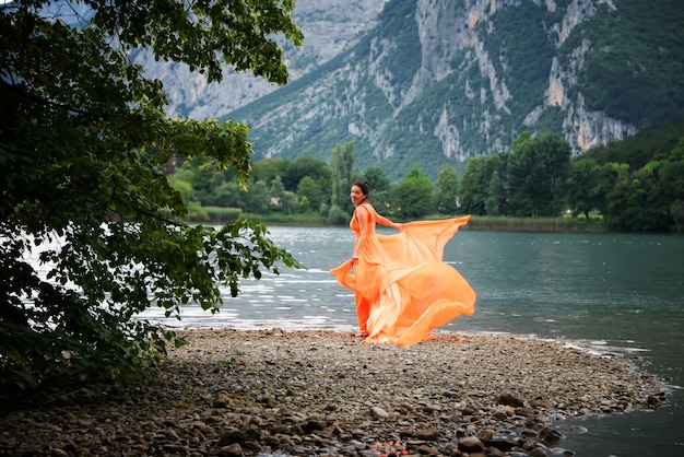 Belle fille en robe orange flottant incroyable avec lagon et montagnes en arrière-plan