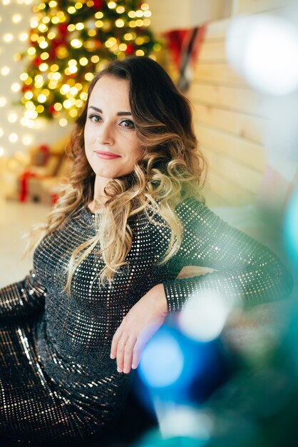 Belle fille en robe de soirée assise sur le fond des décorations de Noël