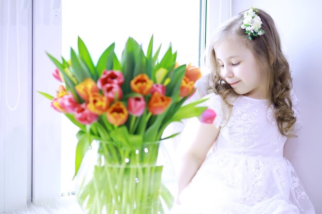 Belle fille en robes blanches avec un magnifique bouquet des premières tulipes Journée internationale de la femme Fille avec des tulipes