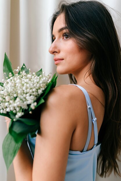 Belle fille romantique en vêtements de nuit posant avec des fleurs