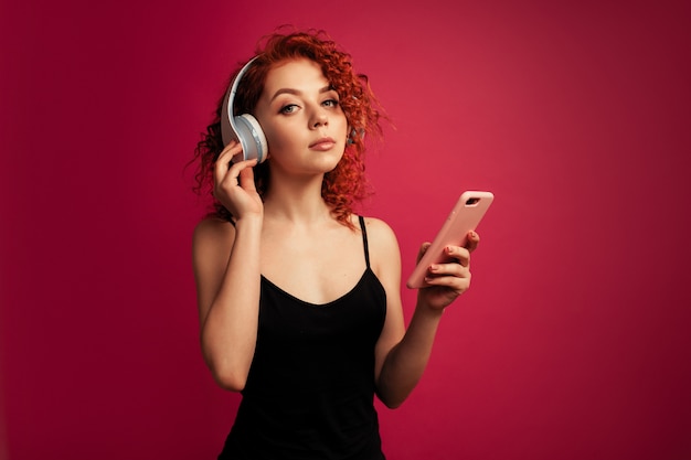 Belle fille rousse au gros casque blanc avec téléphone à la main, écouter de la musique