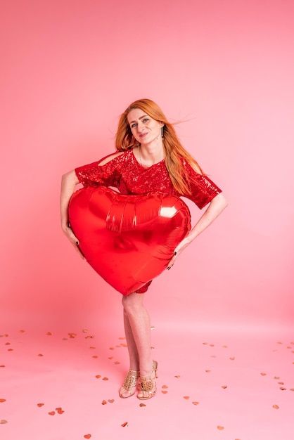 Belle fille rousse avec ballon coeur rouge posant. Concept de la Saint-Valentin heureuse