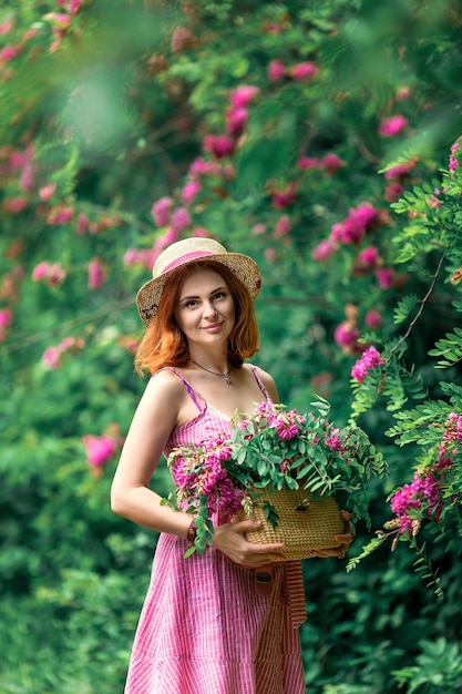 La belle fille rousse naturelle tient le panier de mains avec des fleurs de jardin