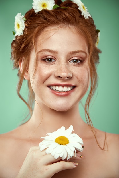 Belle fille rousse positive avec une couronne de camomille sur sa tête