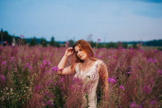 Belle fille rousse vêtue d'une robe dans un champ de fleurs de thé au saule.