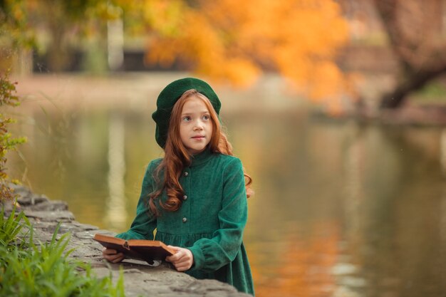 belle fille rousse vêtue d'une robe verte et se promener à l'automne dans le parc avec un livre