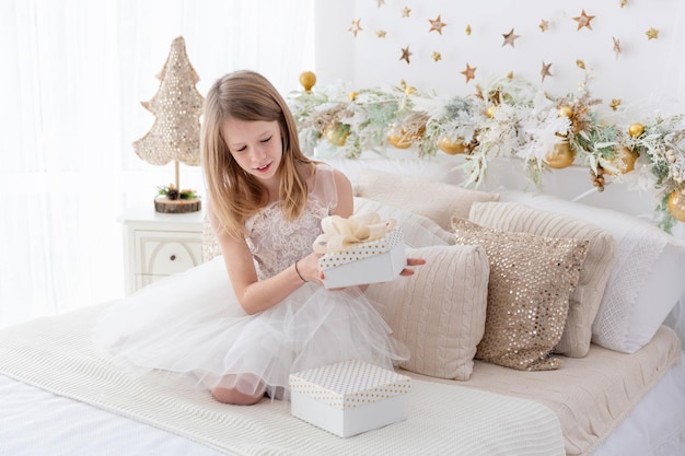 Belle fille s'asseyant sur le lit ouvrant des cadeaux de Noël