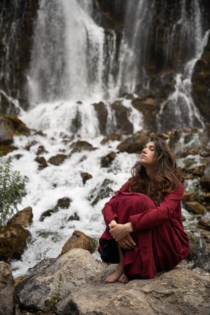 La belle fille s'assied et apprécie la vue de la cascade