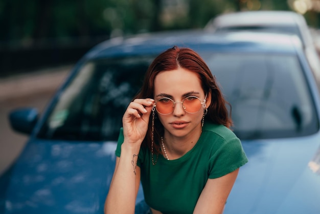 La belle fille s'assied sur le capot d'une voiture bleue