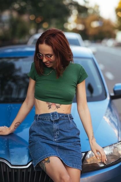 La belle fille s'assied sur le capot d'une voiture bleue