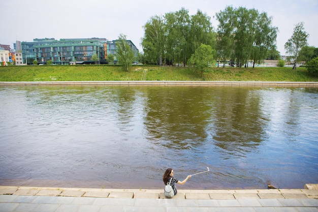 La belle fille s'assied et fait le selfie près de la rivière