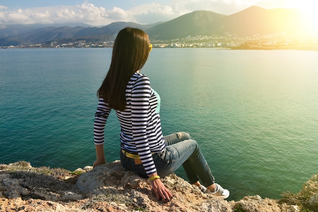 La belle fille s'assied sur la roche et regarde la mer