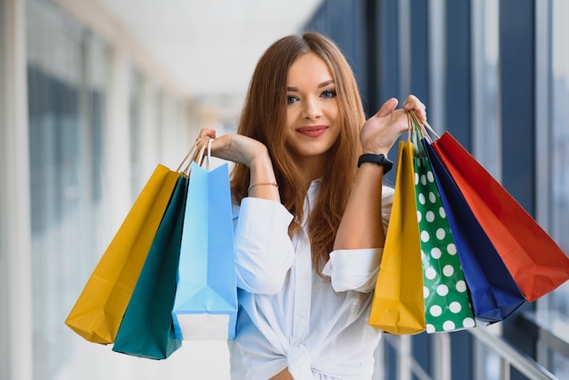 Belle fille avec des sacs à provisions regarde la caméra et sourit tout en faisant du shopping dans le centre commercial