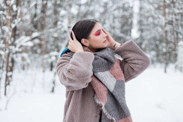 Belle fille scandinave dans des vêtements chauds d'hiver à la mode avec manteau, écharpe marchant dans une forêt d'hiver enneigée