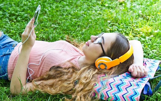 Belle fille se détendre et écouter de la musique dans les écouteurs dans le parc