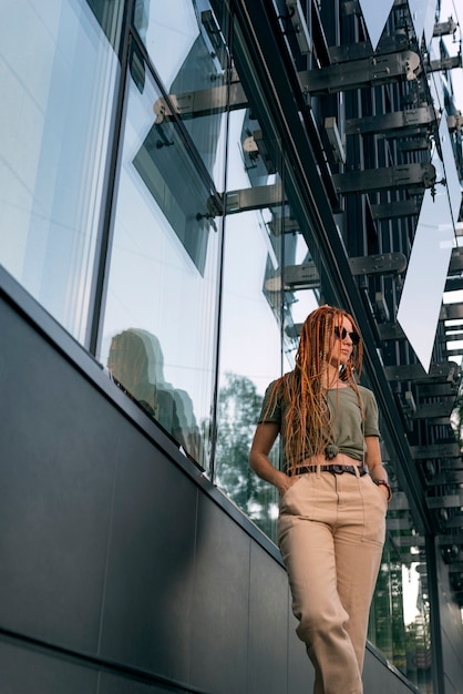 Belle fille se dresse dans le contexte d'un immeuble de bureaux tenant ses mains dans ses poches. Photographie de rue