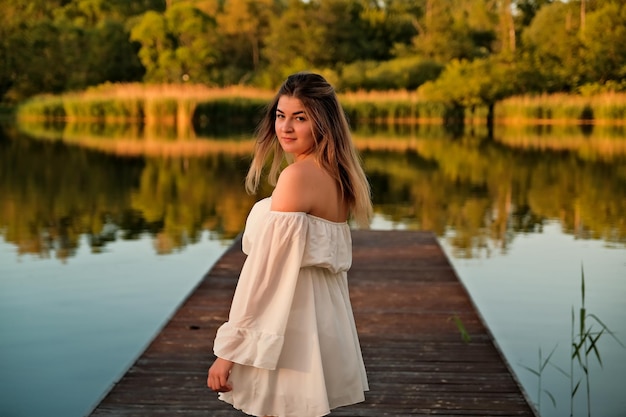 Une belle fille se tient sur la jetée en arrière-plan il y a une rivière un lac