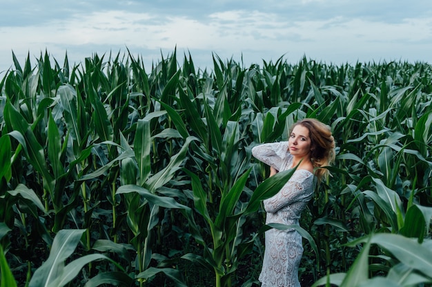 Belle fille se trouve dans le champ de maïs jeune. Agriculture.