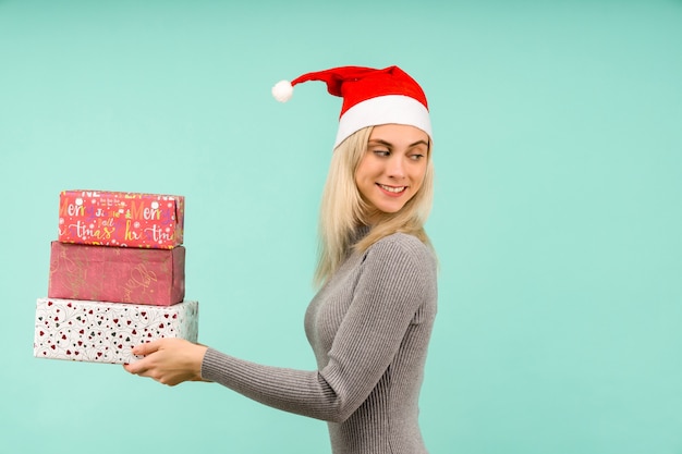 Une belle fille sexy dans un chapeau de nouvel an et une robe grise, tenir en mains des cadeaux Célébration de Noël ou du nouvel an sur fond bleu