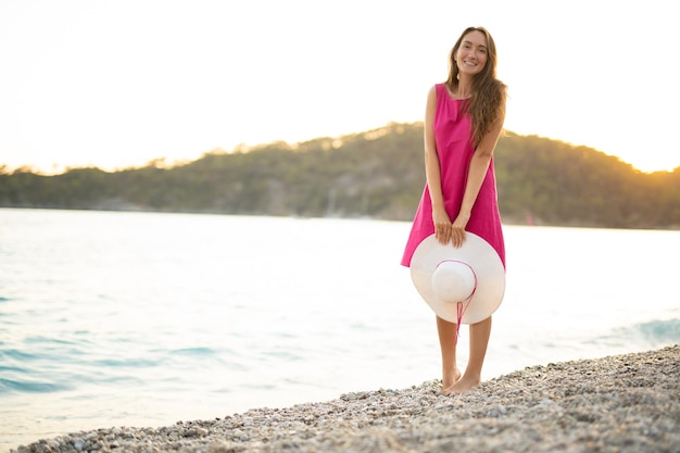 Une belle fille sexy dans une robe rose se reposant sur la plage au coucher du soleil