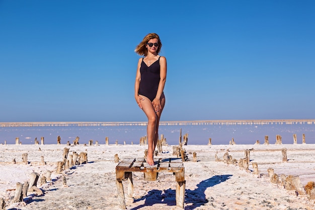 Belle fille sexy en maillot de bain noir posant sur un lac salé rose. Séance photo d'une fille bronzée sur un lac rose salé