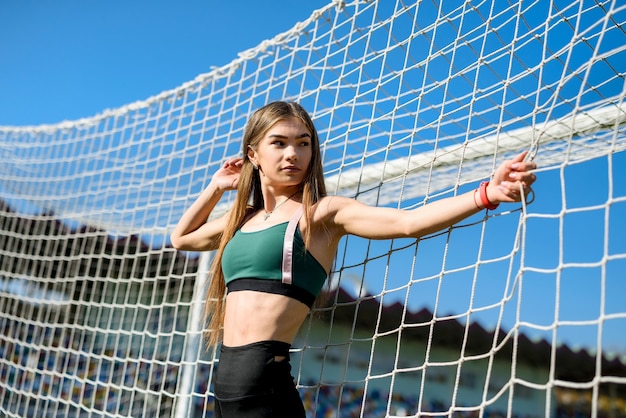 Une belle fille avec une silhouette parfaite se tient près d'un but de football au stade. Concept de remise en forme et de mode de vie sain.