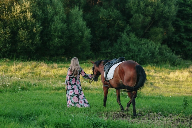 Belle fille avec son cheval sur une belle prairie éclairée par une lumière chaude