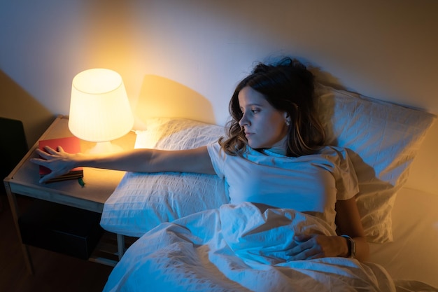 Belle fille souffrant d'insomnie saisissant un livre à lire au milieu de la nuit Acte de nuit