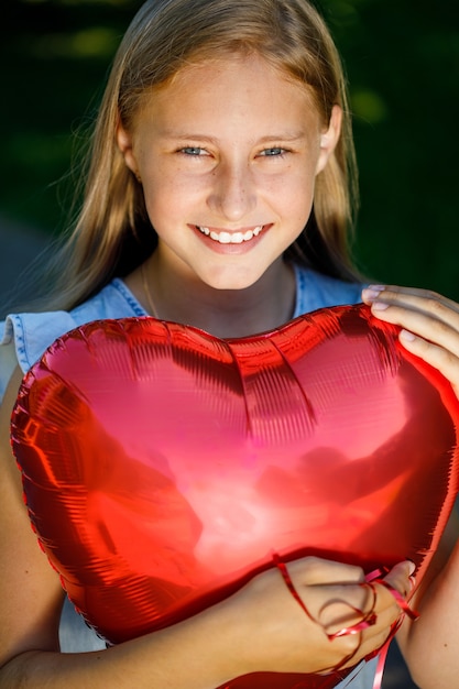 Belle fille souriante avec un ballon en forme de coeur dans la nature