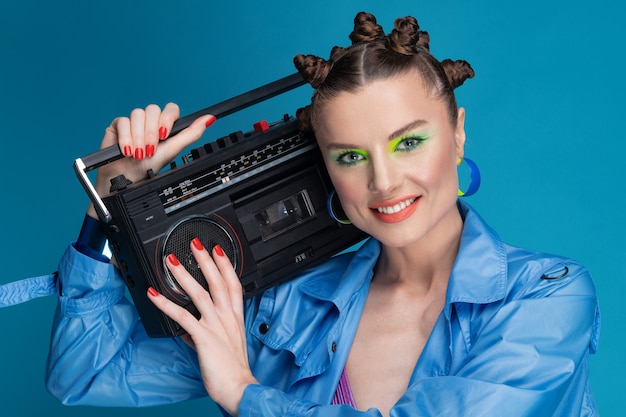 Photo belle fille souriante avec des cheveux élégants et du maquillage détient boombox