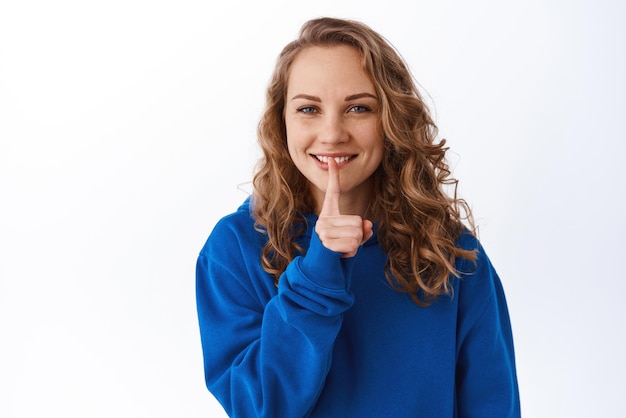 Belle fille souriante chut demandant de se taire avec une expression de visage heureux chut faisant signe chut pour garder le secret debout sur fond blanc