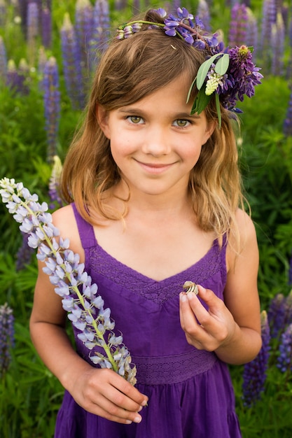 Belle fille souriante dans une robe violette avec une couronne de lupins