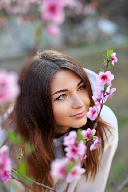 Belle fille souriante debout près d'un pêcher pendant le coucher du soleil Visage heureux Temps de printemps