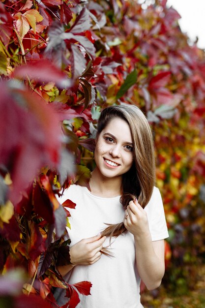 Belle fille souriante heureuse aux cheveux longs, posant dans le contexte des feuilles d'automne dans le parc.