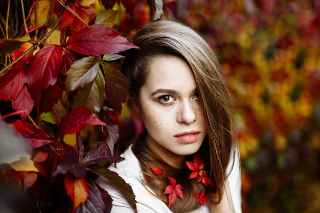 Belle fille souriante heureuse aux cheveux longs, posant dans le contexte des feuilles d'automne dans le parc.