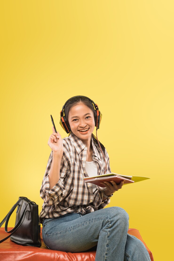 Photo belle fille souriante portant des écouteurs tenant un stylo et un livre tout en regardant la caméra